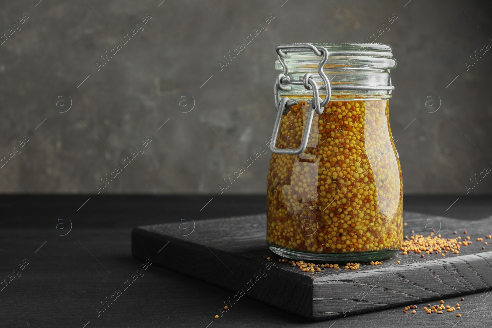 Photo of Whole grain mustard in jar and dry seeds on black table. Space for text