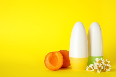 Photo of Female roll-on deodorants, apricots and chamomile flowers on yellow background, space for text