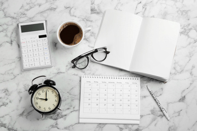 Flat lay composition with calendar and cup of coffee on white marble table