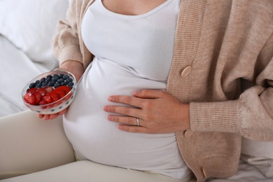 Photo of Pregnant woman eating yogurt with berries on bed, closeup. Healthy diet
