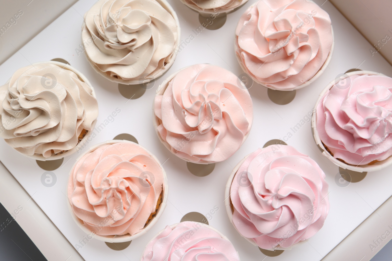 Photo of Many tasty cupcakes with colorful cream in box, top view