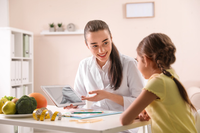 Photo of Professional nutritionist with tablet consulting little girl in office