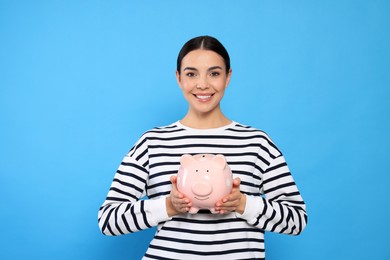 Photo of Happy young woman with piggy bank on light blue background