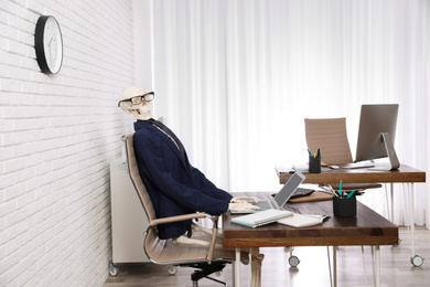 Human skeleton in suit using laptop at table in office