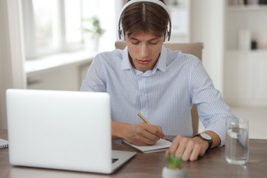 Man in headphones taking notes during webinar at wooden table in office