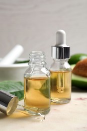 Photo of Bottle of essential oil, pipette and fresh avocado on table, closeup