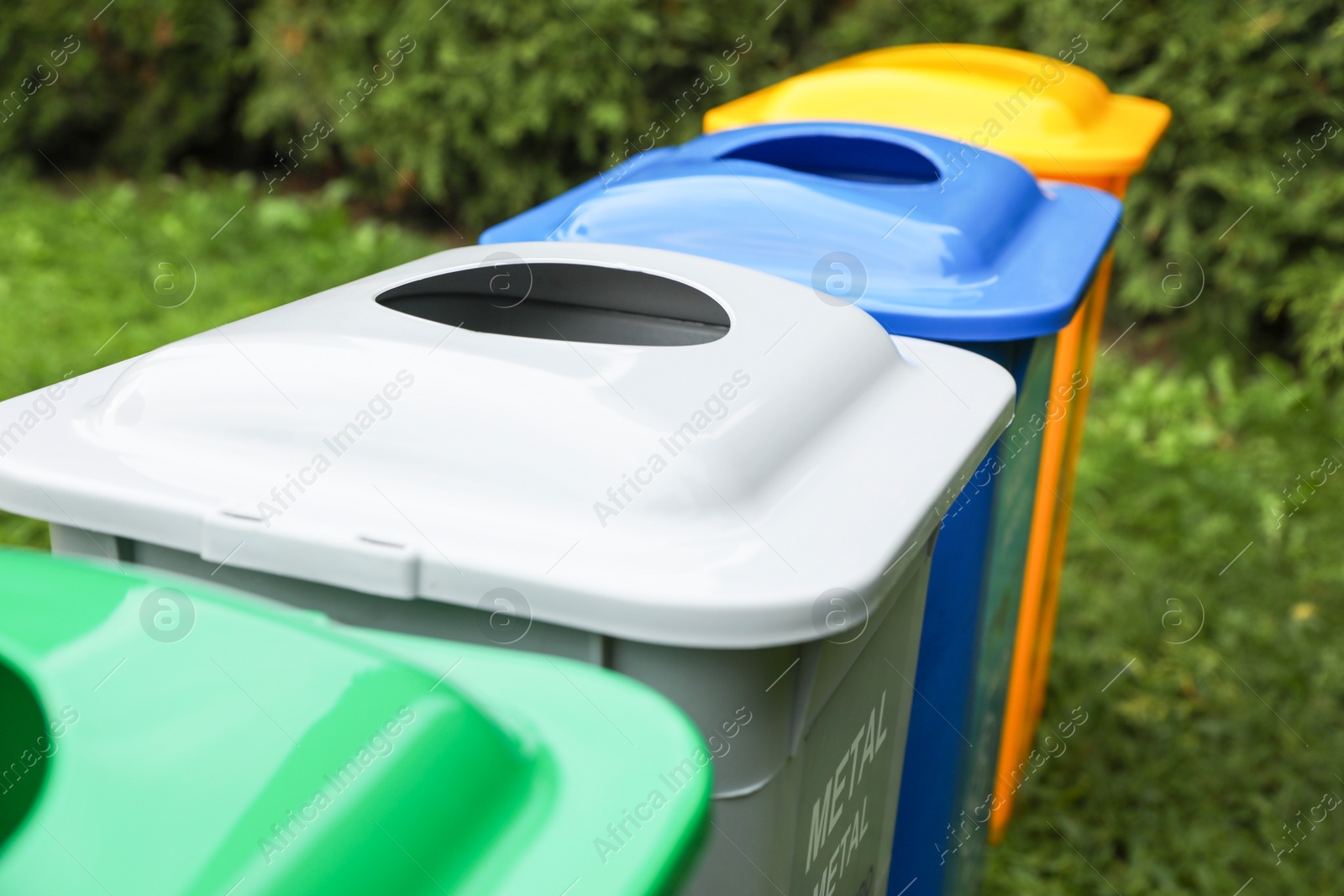 Photo of Many color recycling bins on green grass outdoors, closeup