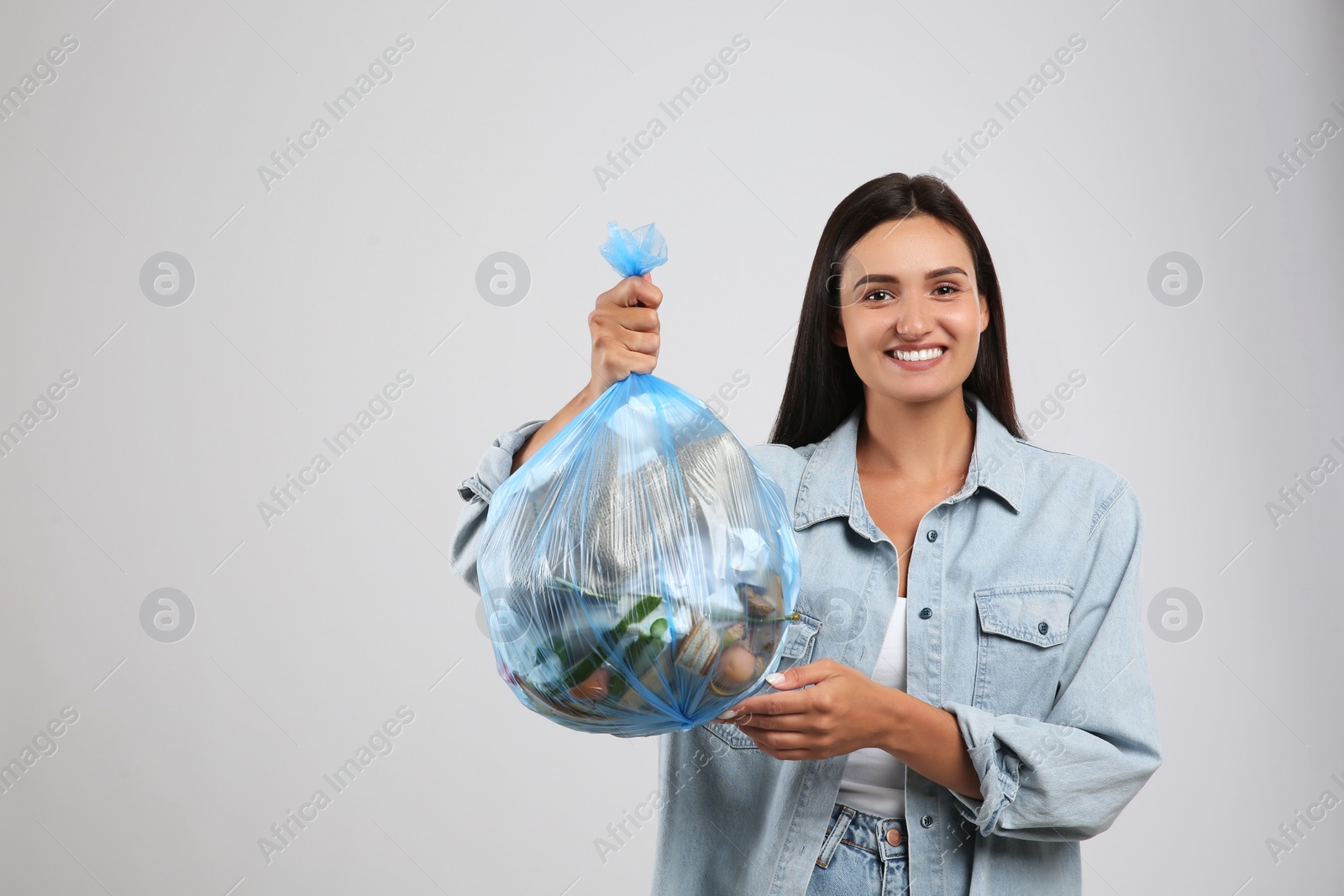 Photo of Woman holding full garbage bag on light background