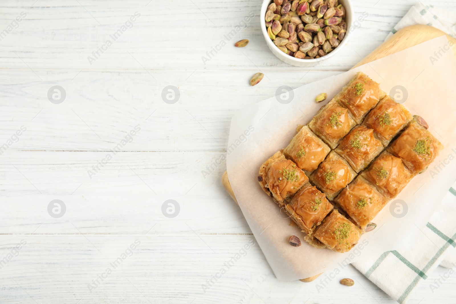 Photo of Delicious sweet baklava with pistachios on white wooden table, flat lay. Space for text