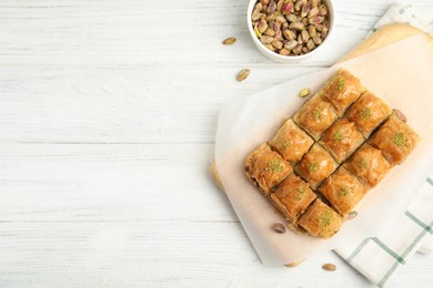 Photo of Delicious sweet baklava with pistachios on white wooden table, flat lay. Space for text