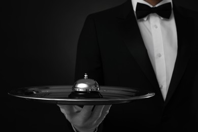 Photo of Butler holding metal tray with service bell on black background, closeup