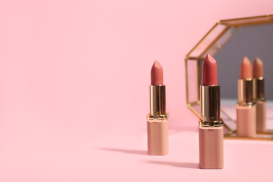Photo of Different lipsticks near mirror on pink background, space for text