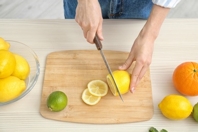 Photo of Woman cutting fruit for making natural detox lemonade at table, closeup