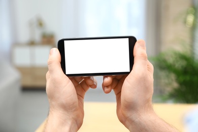 Man holding smartphone with blank screen indoors, closeup of hands. Space for text