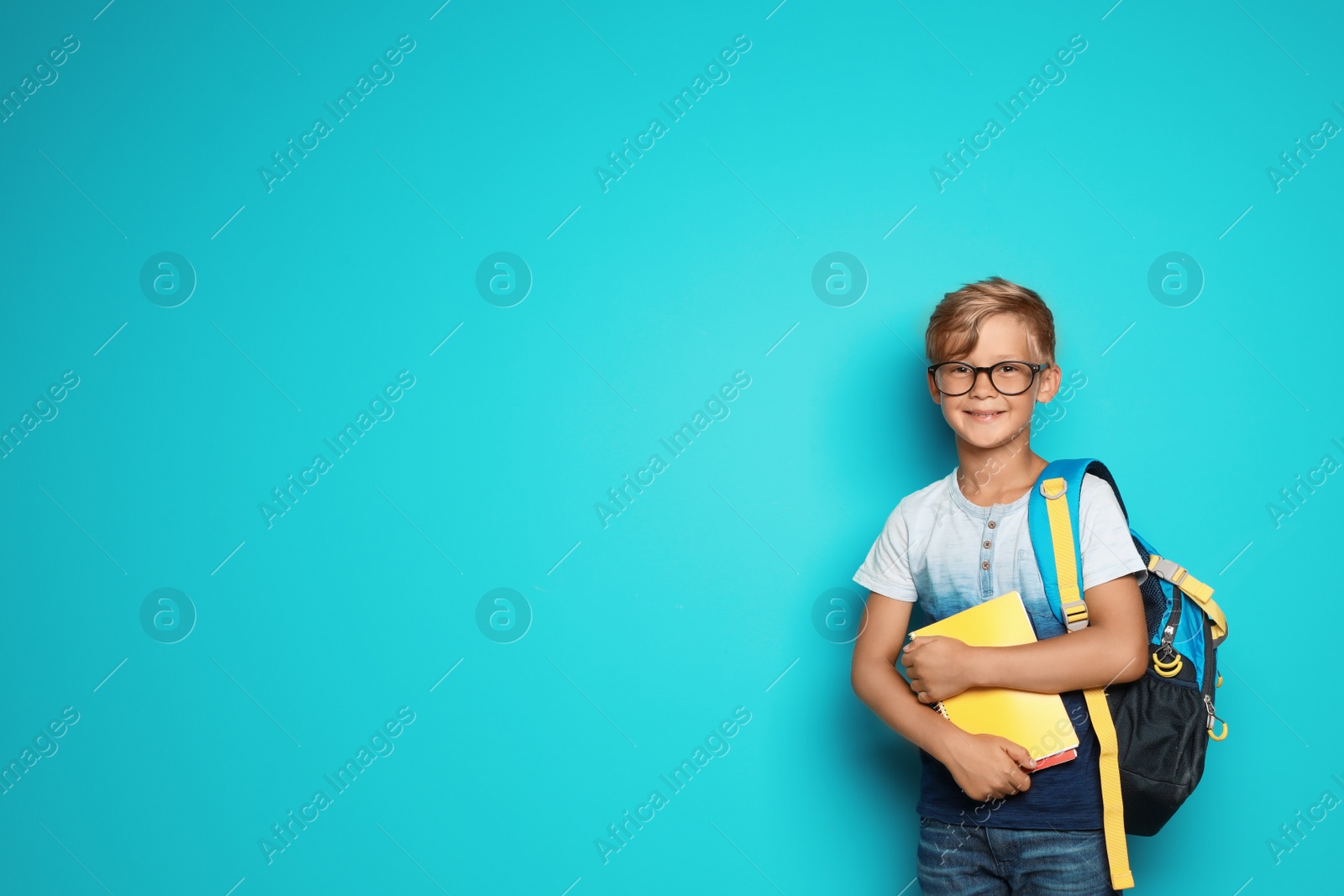 Photo of Little school child with backpack and copybooks on color background