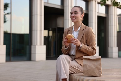 Photo of Happy businesswoman with hamburger having lunch on bench outdoors