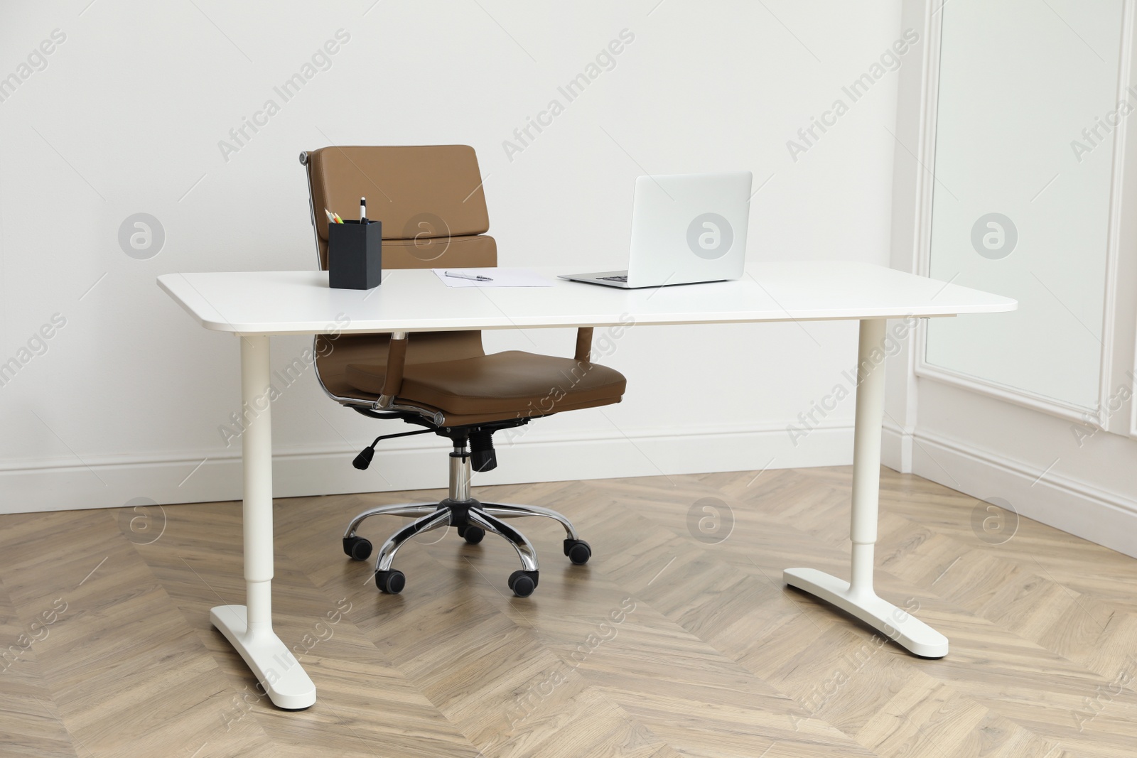 Photo of Stylish workplace with laptop and comfortable armchair near white wall indoors. Interior design