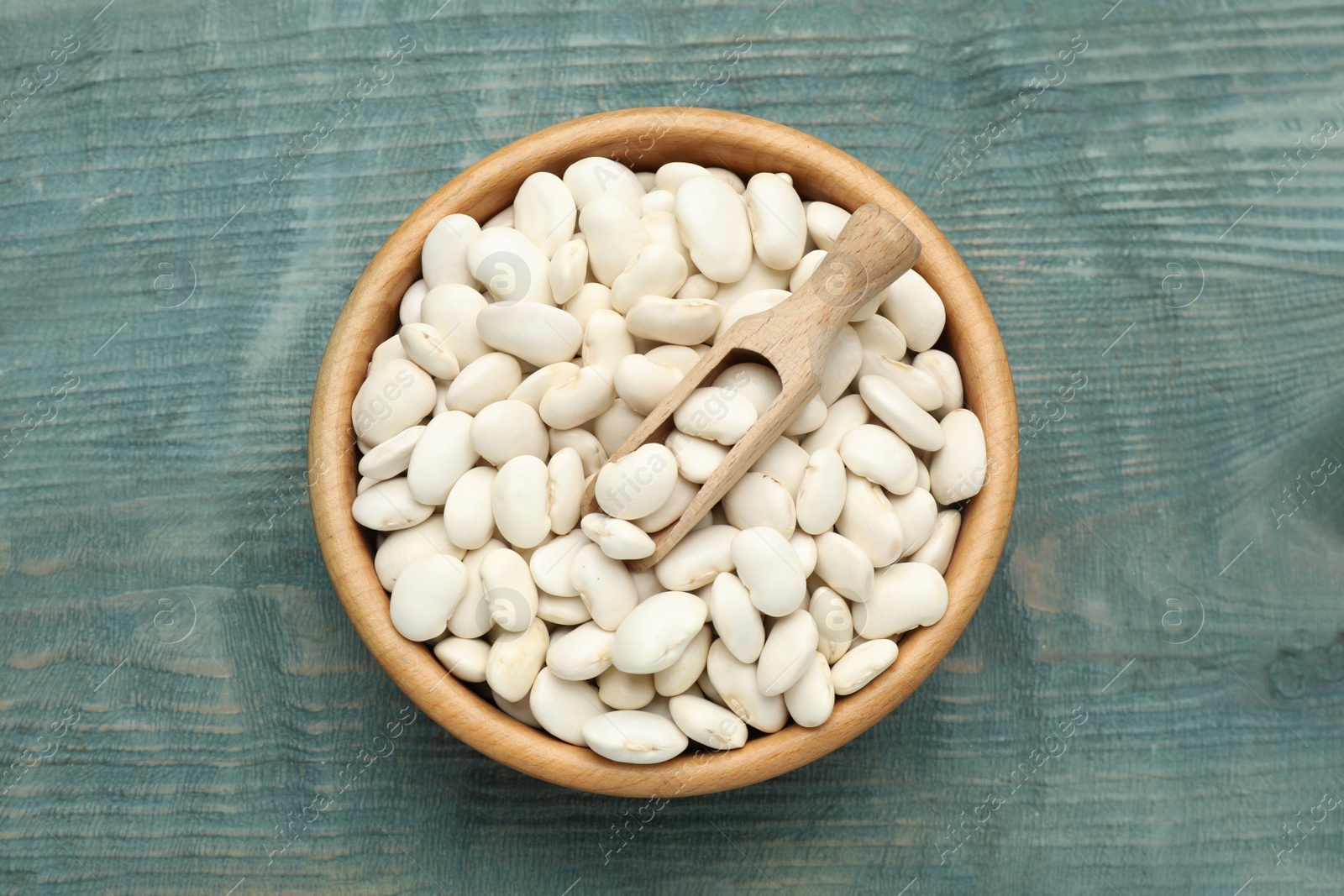 Photo of Bowl and scoop with uncooked white beans on blue wooden table, top view