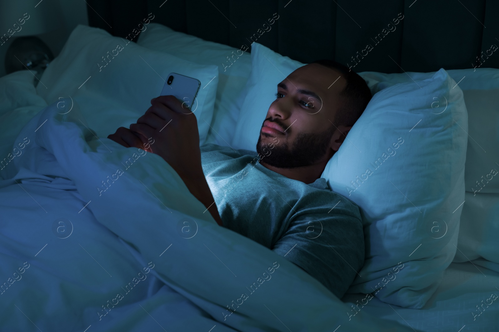 Photo of Young man using smartphone in bed at night. Internet addiction