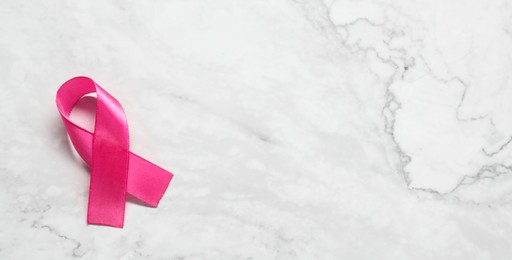 Pink ribbon on white marble table, top view and space for text. Breast cancer awareness