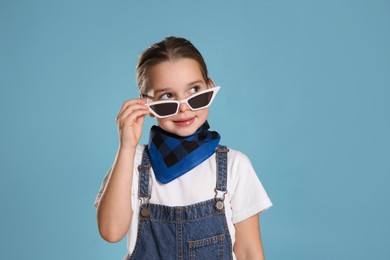 Photo of Cute little girl wearing stylish bandana and sunglasses on turquoise background