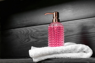Photo of Glass soap dispenser and towel on table. Space for text