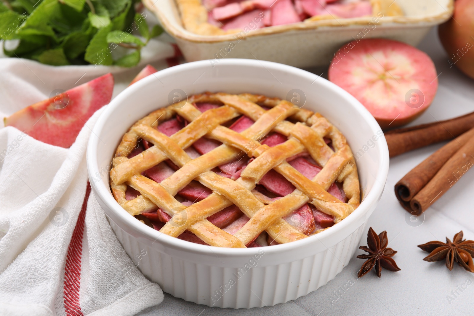 Photo of Baking dish with delicious apple pie and ingredients on white tiled table