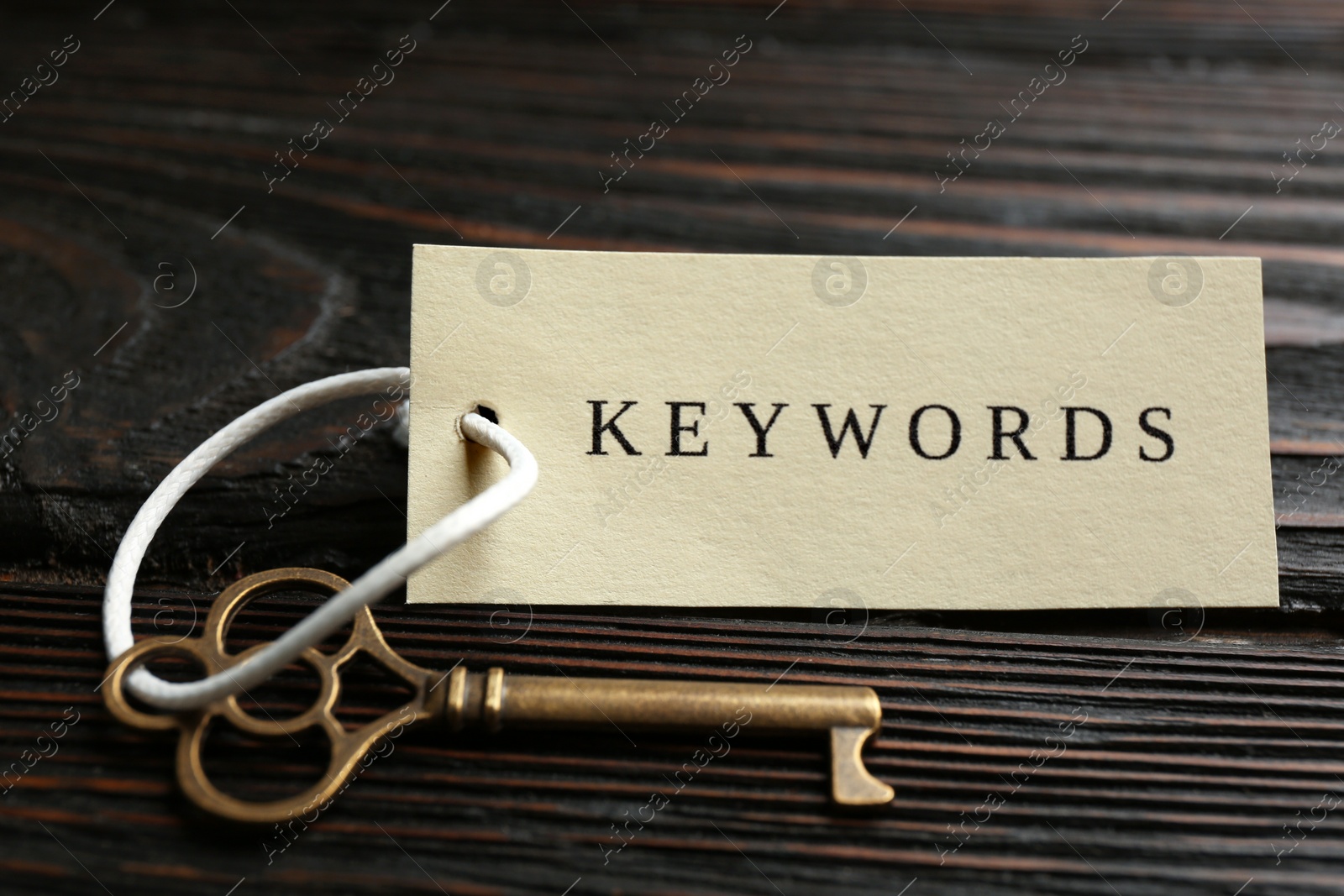 Photo of Key with tag KEYWORDS on wooden background, closeup