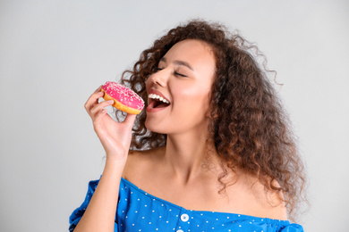 Photo of Beautiful African-American woman with donut on light grey background