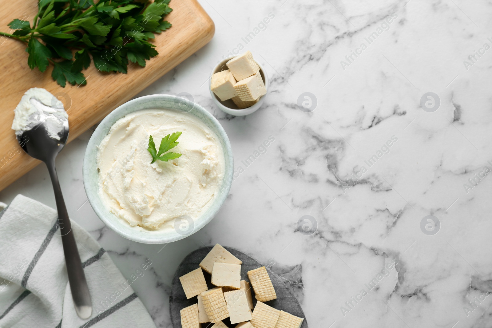 Photo of Delicious tofu cheese with parsley and spoon on white marble table, flat lay. Space for text