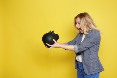 Photo of Emotional young woman with piggy bank on color background. Space for text