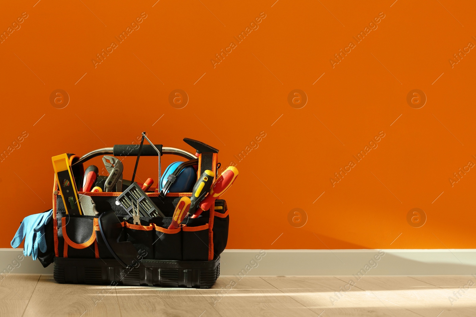 Photo of Bag with different tools for repair on floor near orange wall. Space for text