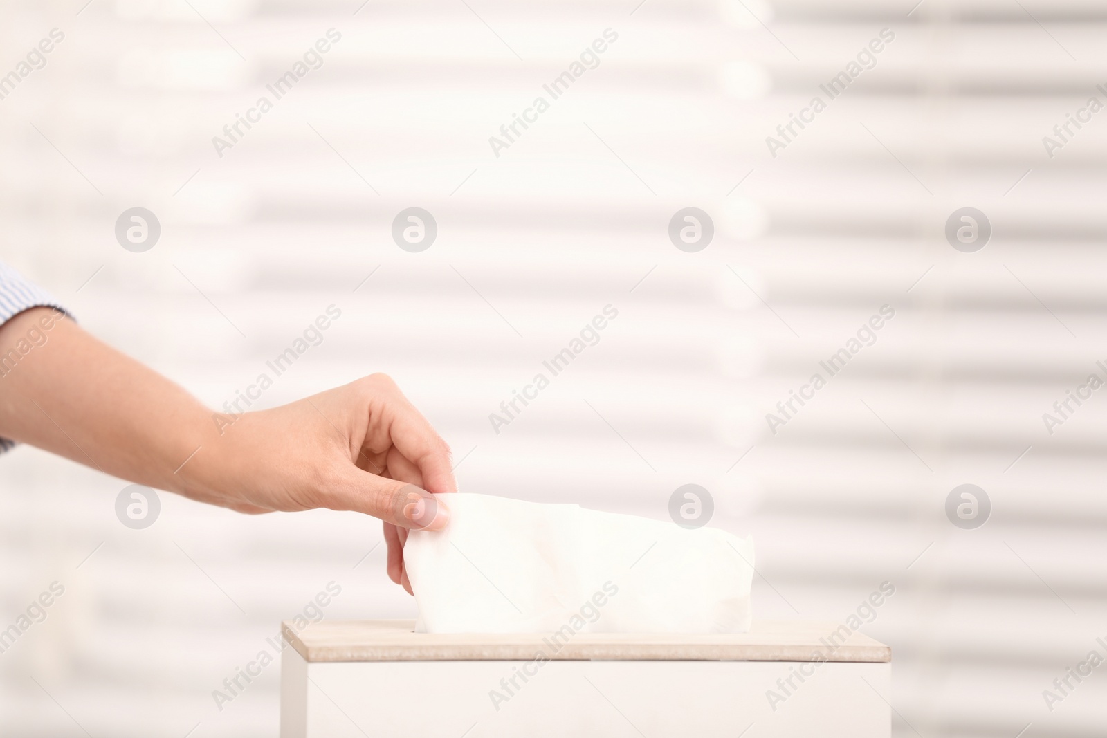 Photo of Woman taking paper tissue from holder on light background, closeup. Space for text