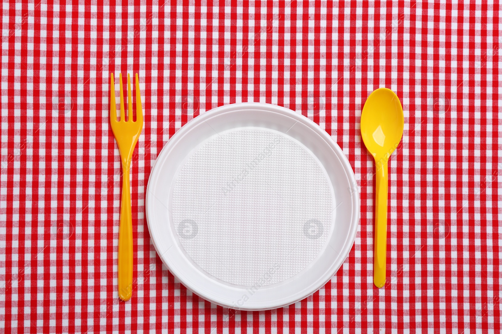 Photo of Table setting with plastic dishware on plaid fabric, flat lay