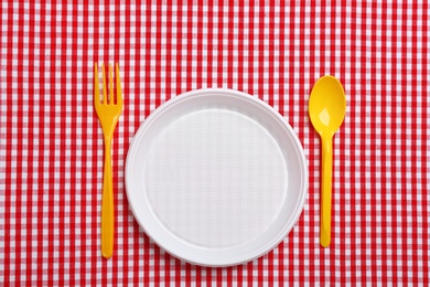 Photo of Table setting with plastic dishware on plaid fabric, flat lay