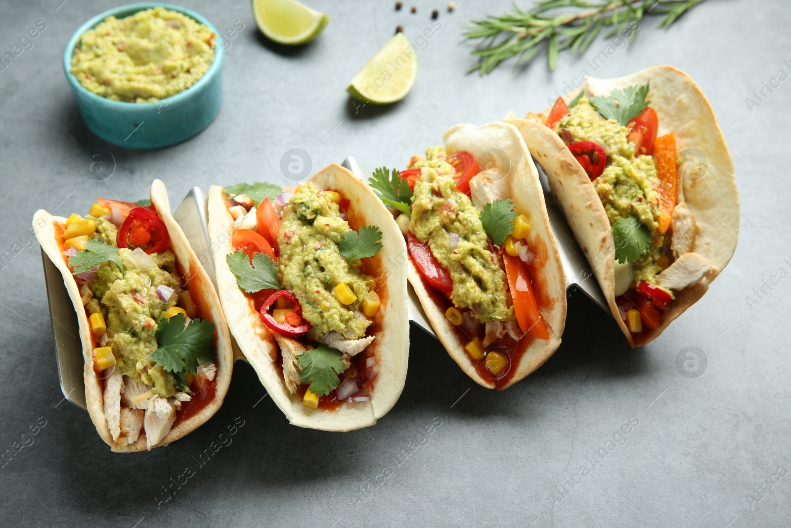 Photo of Delicious tacos with guacamole, meat and vegetables on grey table, closeup