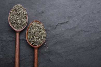 Photo of Spoons with dried thyme on black table, flat lay. Space for text