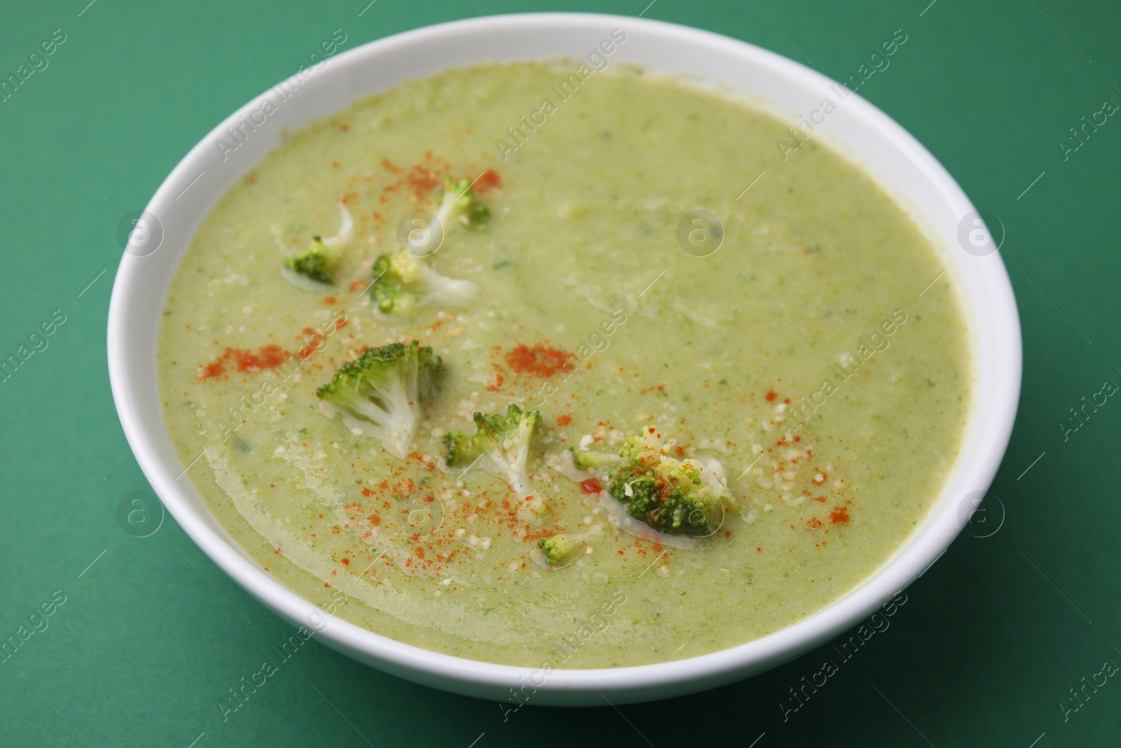 Photo of Delicious broccoli cream soup on green background, closeup