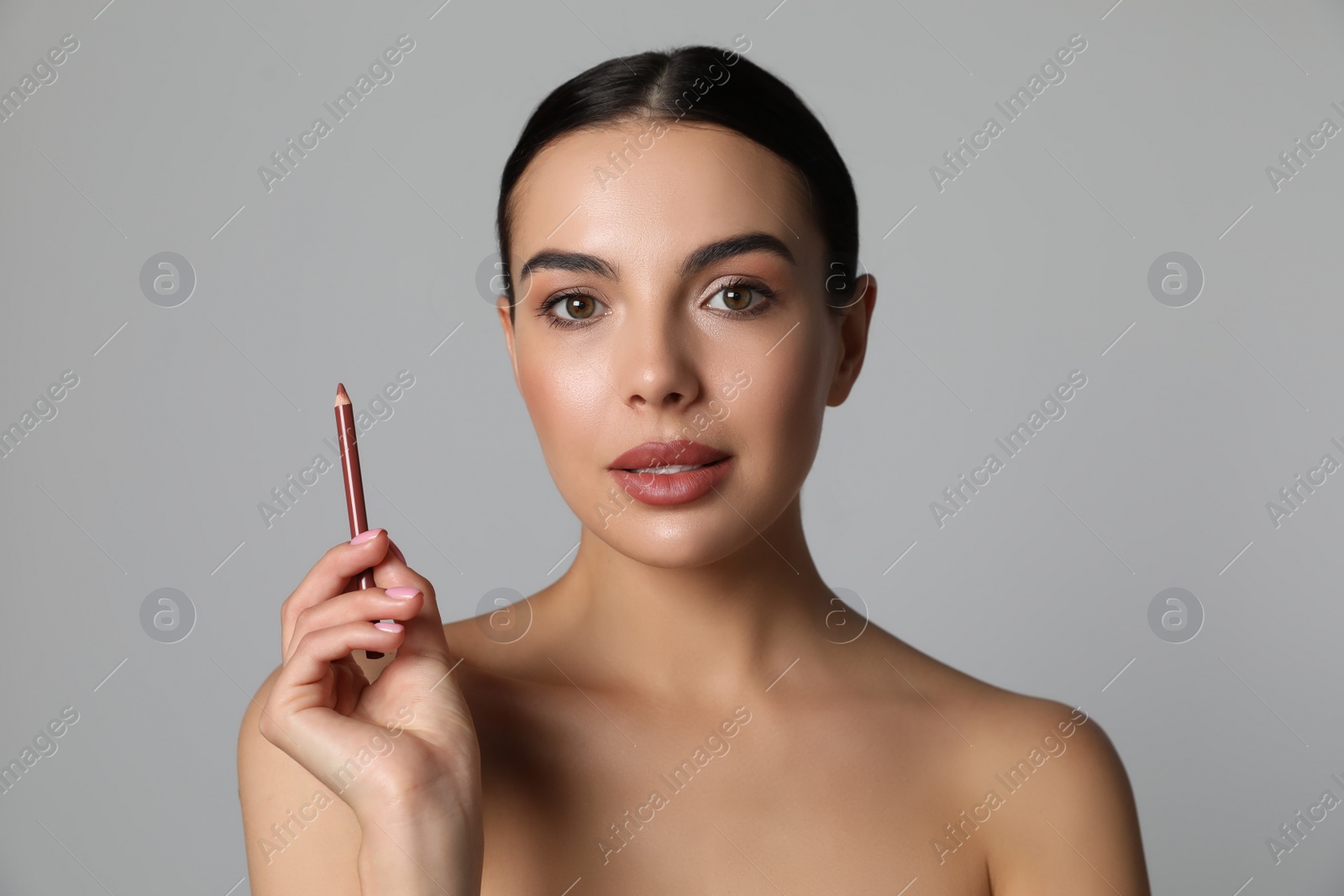 Photo of Pretty young woman with beautiful nude lip pencil on grey background