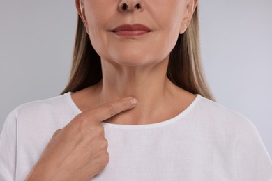 Endocrine system. Senior woman doing thyroid self examination on light grey background, closeup