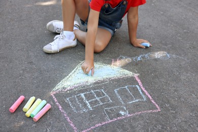 Little child drawing house with colorful chalk on asphalt, closeup