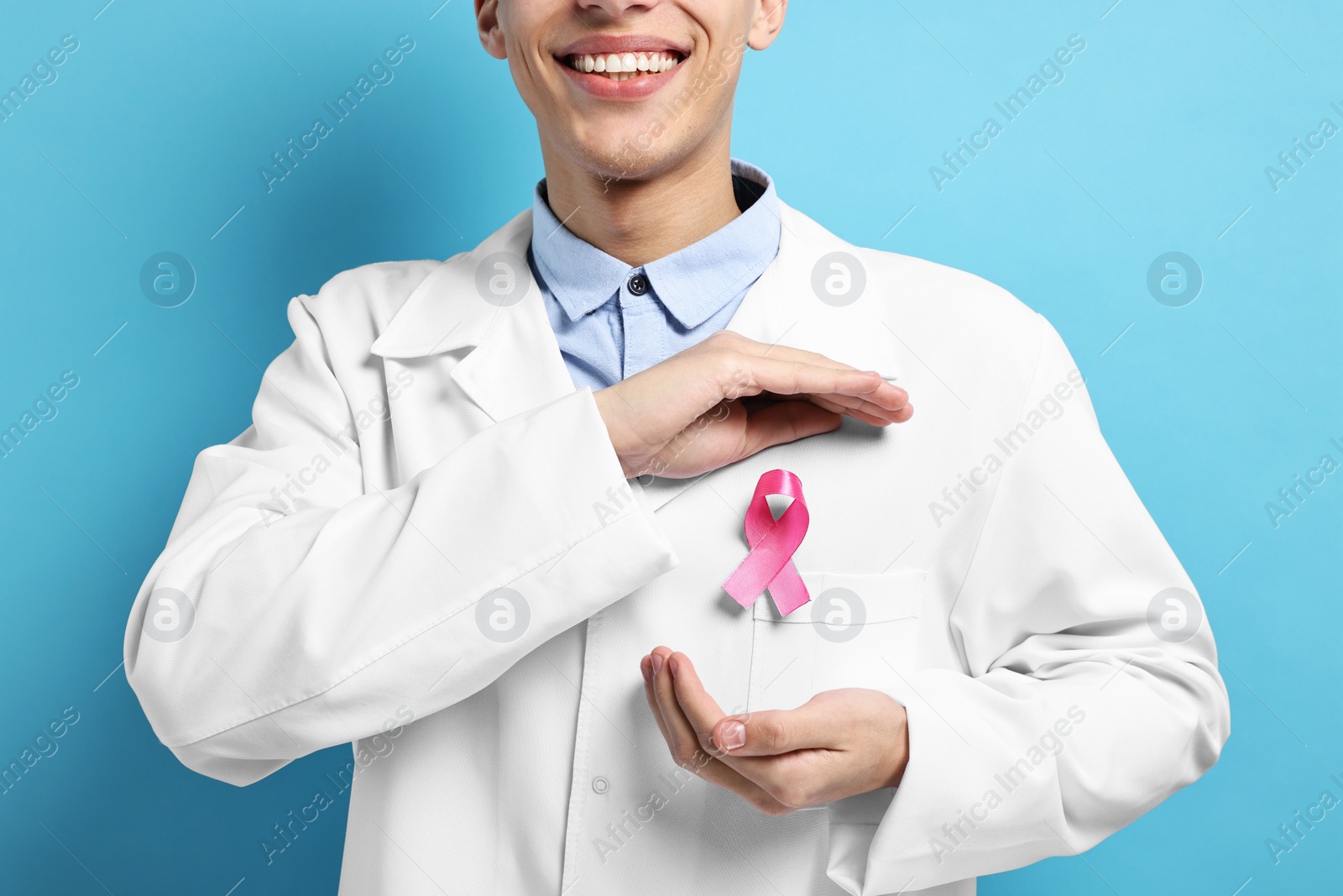 Photo of Mammologist with pink ribbon on light blue background, closeup. Breast cancer awareness