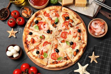 Photo of Tasty pizza with seafood and ingredients on black table, flat lay