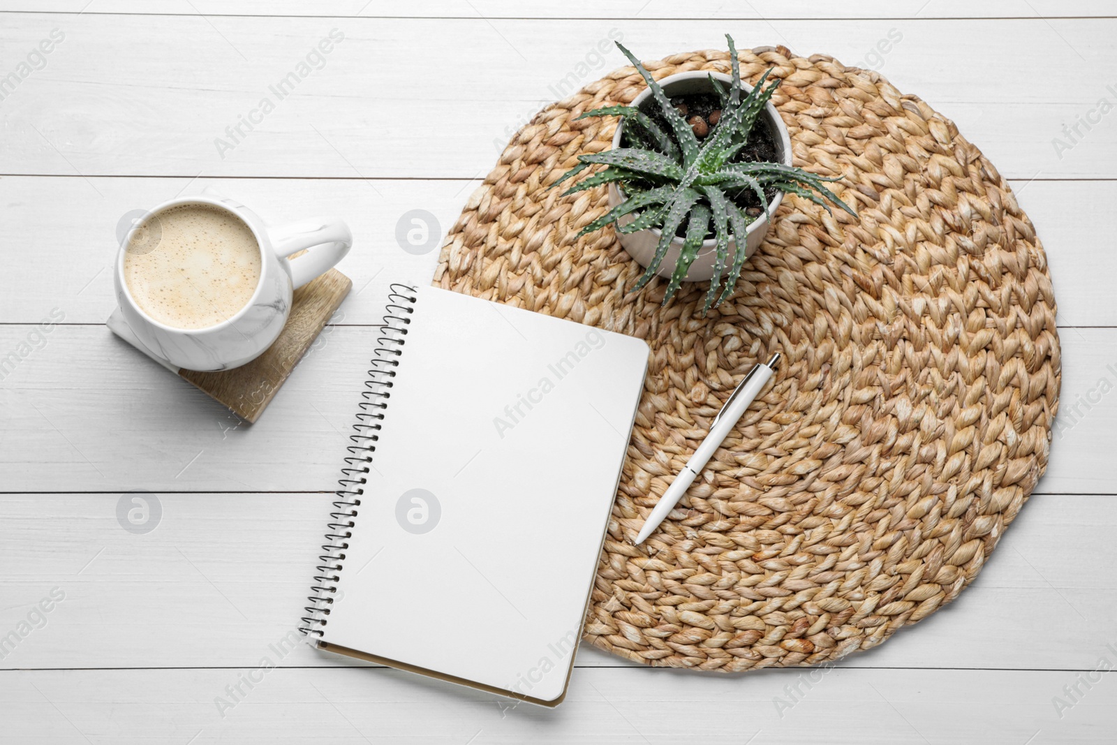 Photo of Mug of coffee with stylish cup coaster, houseplant and notebook on white wooden table, flat lay
