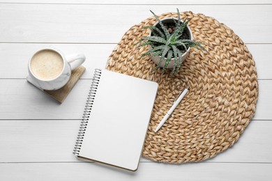 Mug of coffee with stylish cup coaster, houseplant and notebook on white wooden table, flat lay
