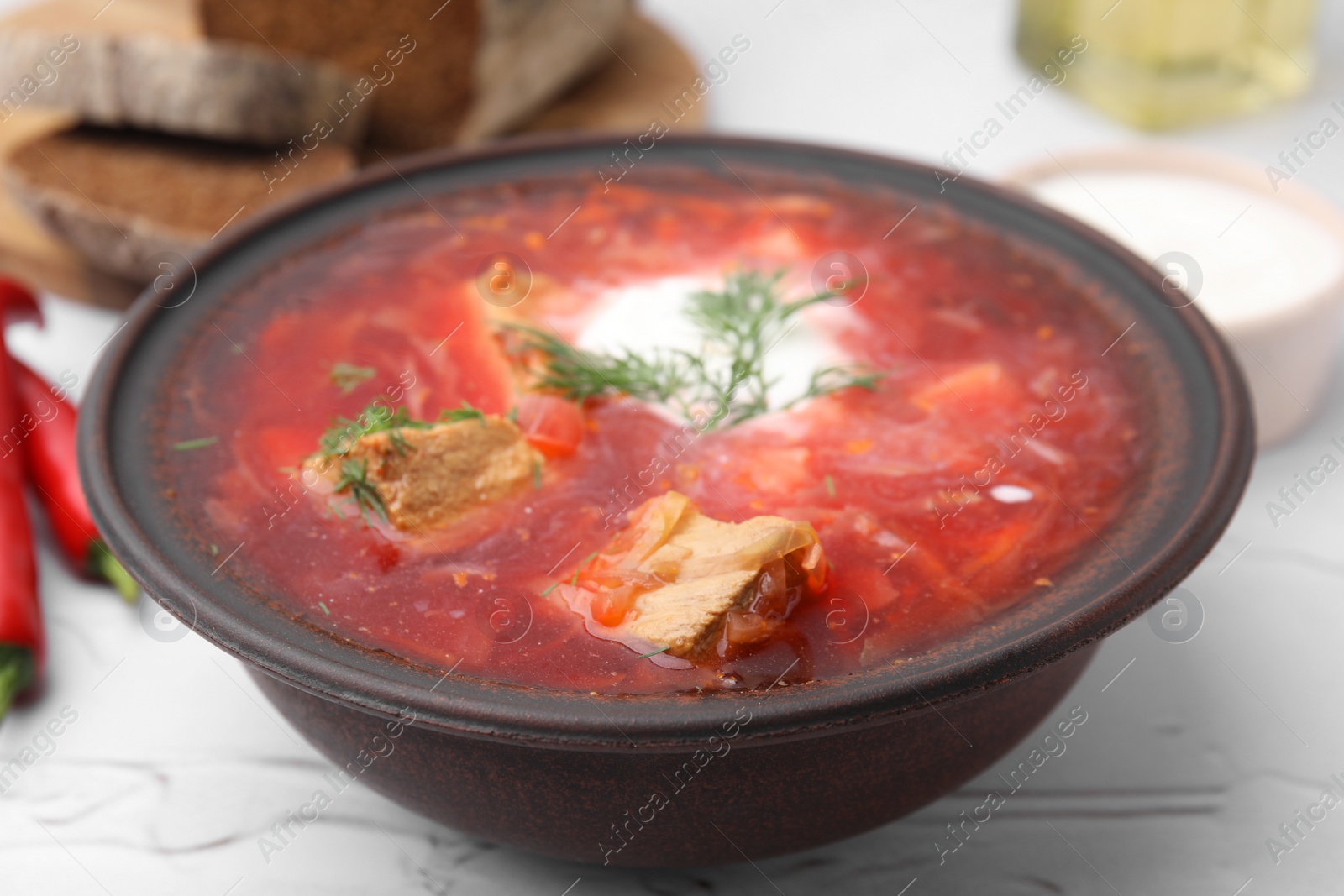 Photo of Tasty borscht with sour cream in bowl on white textured table, closeup