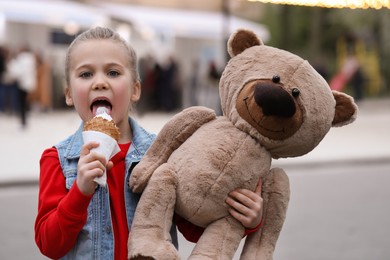 Photo of Little girl with teddy bear eating ice cream outdoors