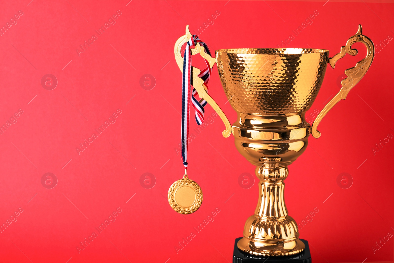 Photo of Golden trophy cup and medal on red background. Space for text