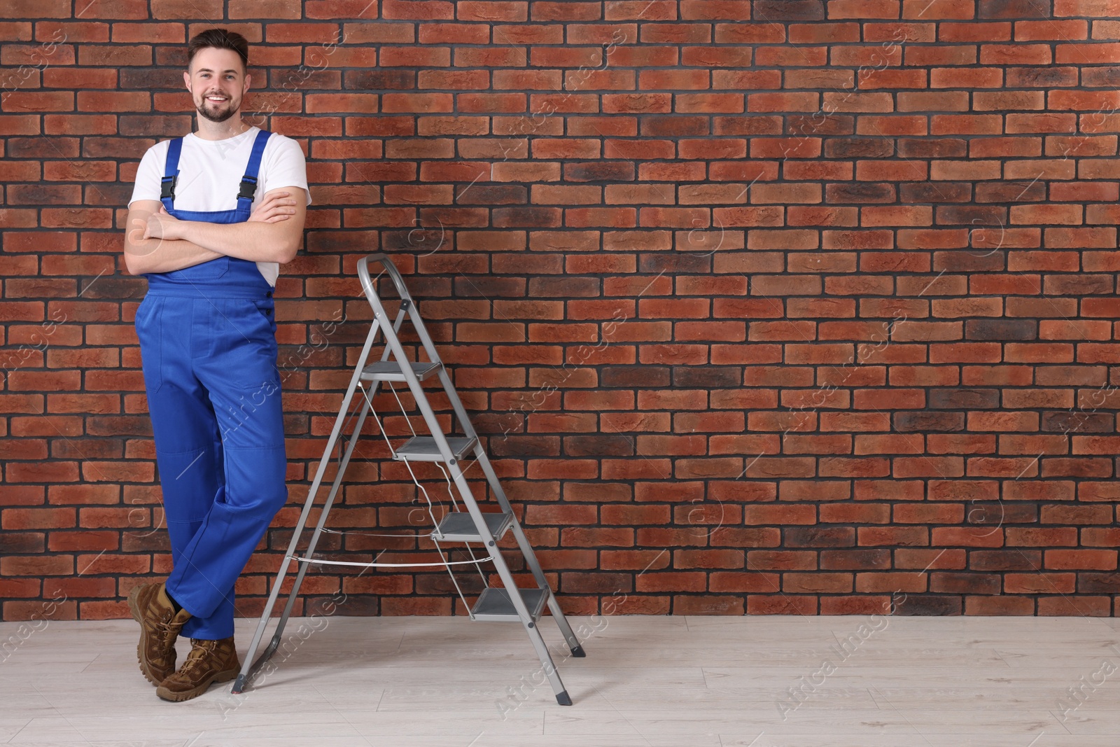 Photo of Happy worker near stepladder against brick wall indoors, space for text
