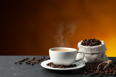 Cup of hot aromatic coffee and roasted beans on black table against brown background. Space for text